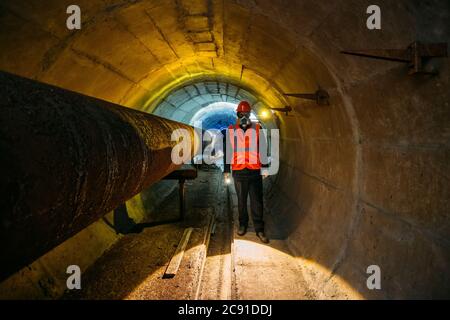 Le travailleur du tunnel examine le pipeline dans le tunnel souterrain Banque D'Images