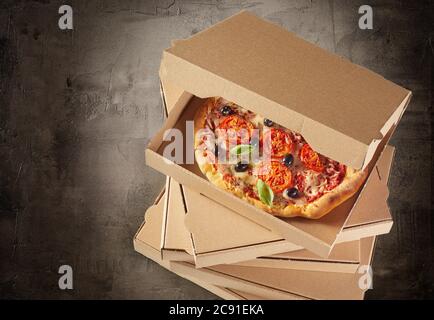 Boîtes en carton marron générique empilées avec une savoureuse pizza italienne fraîche à l'intérieur de la boîte ouverte de dessus vue grand angle sur l'ardoise avec vignette Banque D'Images