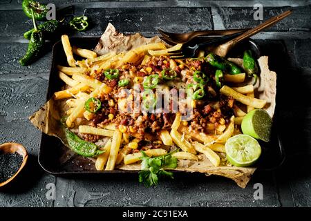 Frites de pommes de terre nappées de viande hachée, poivrons épicés frais et fromage servis avec des limes dans une double portion avec une vue panoramique Banque D'Images