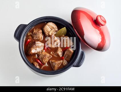 Délicieux goulash de bœuf allemand dans une sauce épicée avec piments et feuilles de Laurier dans une vue de dessus en bas servi dans une petite casserole en fonte sur blanc avec rouge Banque D'Images