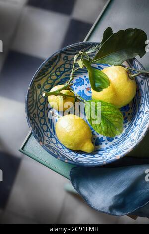 Citrons tropicaux frais avec feuilles vertes sur une branche dans un bol en poterie rustique bleu et blanc vu d'en haut sur le coin d'une table Banque D'Images