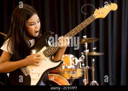 Une jeune fille asiatique mignonne d'école élémentaire avec de longs cheveux jouant avec une guitare électrique sérieuse dans des chansons de rock. Banque D'Images