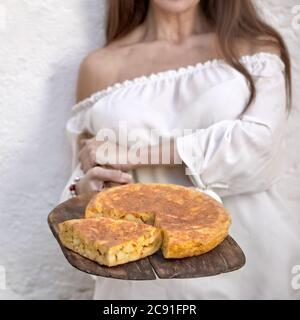 Place gros plan sur une tortilla de patatas fraîchement cuite sur une pagaie en bois vintage tenue par une jeune femme en haut blanc Banque D'Images