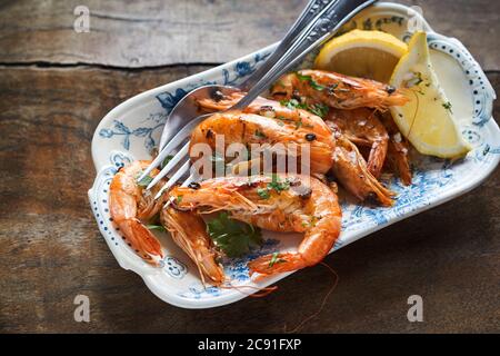 Hors-d'œuvre de fruits de mer de crevettes grillées entières épicées assaisonnées d'herbes hachées servies sur une assiette vintage sur une table en bois rustique avec vue au plafond Banque D'Images