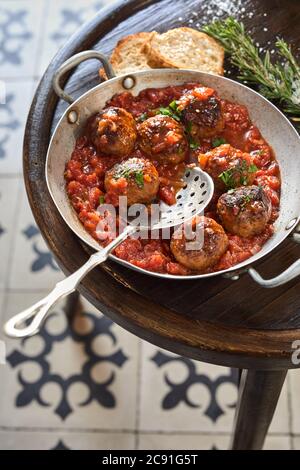 Boulettes de viande espagnoles dans une sauce épicée aux tomates et aux herbes fraîches, servies à l'extérieur dans un wok rustique sur une petite table Banque D'Images