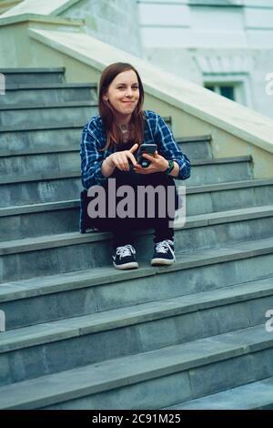 Jeune femme assise sur les escaliers du manoir avec un smartphone entre les mains. Femme adulte avec téléphone portable assise sur les marches du palais. Banque D'Images