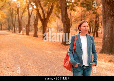 Portrait of businesswoman in autumn park, debout sur sentier entre les arbres avec un feuillage dynamique Banque D'Images