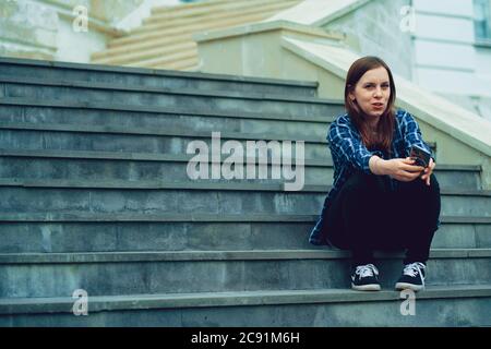 Jeune femme assise sur les escaliers du manoir avec un smartphone entre les mains. Femme adulte avec téléphone portable assise sur les marches du palais. Banque D'Images