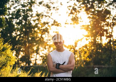 Homme portant un t-shirt blanc de muscle et des lunettes de soleil avec son bras repliés et face droite Banque D'Images