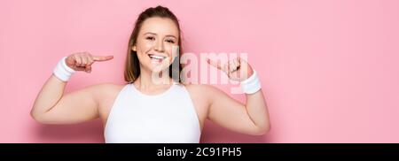 récolte panoramique de gaie en surpoids jeune fille pointant avec les doigts sur elle-même sur rose Banque D'Images