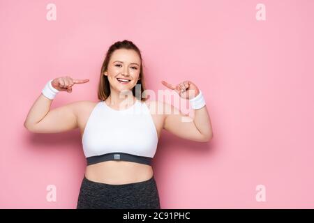 bonne fille en surpoids pointant avec les doigts sur elle-même sur rose Banque D'Images