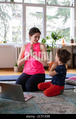 Jeune mère et enfant faisant Namaste poser tout en pratiquant le yoga À la maison, devant l'ordinateur portable
