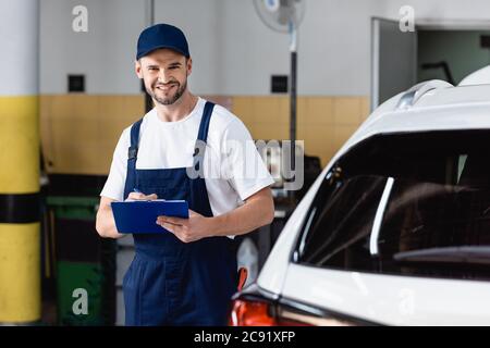 un bon mécanicien en uniforme tenant le presse-papiers près de la voiture moderne Banque D'Images