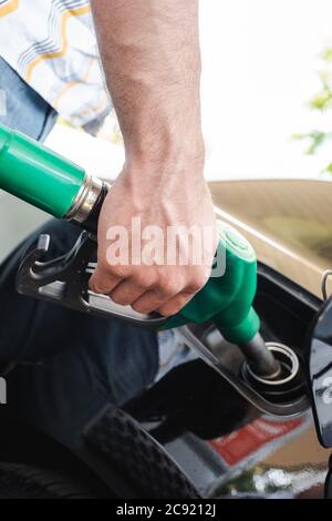 Vue rognée de l'homme tenant la buse de ravitaillement près du couvercle du réservoir de gaz ouvert à l'extérieur Banque D'Images