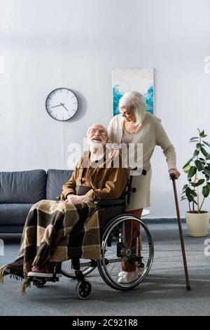 femme âgée avec bâton de marche et homme handicapé en fauteuil roulant souriant tout en regardant l'un l'autre Banque D'Images