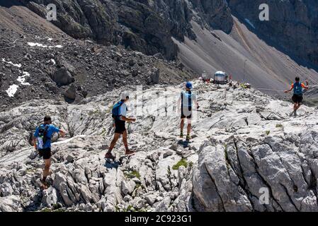 Quatre hommes marchent à travers les rochers vers le refuge de montagne au loin. Banque D'Images