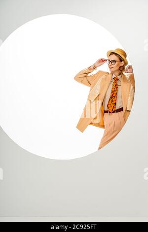 Femme élégante en chapeau de paille et veste beige ajustement de lunettes près du cercle sur fond blanc Banque D'Images