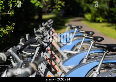 Location de vélos debout dans une rangée à la station de charge à l'extérieur dans le soleil d'été lumineux Banque D'Images