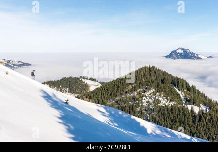 Homme avec deux chiens descendant la montagne enneigée avec une vue incroyable sur les montagnes au-dessus de la couche de brouillard de la vallée de l'inversion. Mer de nuages. Vue de Banque D'Images