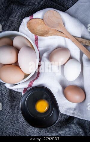 Image de jaune d'œuf dans un bol à côté d'œufs sains dans un plat ou un chiffon blanc et des ustensiles de cuisine. Banque D'Images