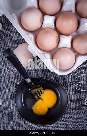 Image de jaune d'œuf dans un bol à côté d'œufs sains dans un plat ou un chiffon blanc et des ustensiles de cuisine. Banque D'Images