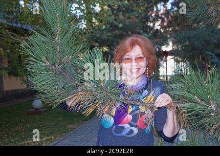 Femme mature dans un chemisier coloré garde en face de lui-même une branche du pin de Crimée avec de longues aiguilles Banque D'Images