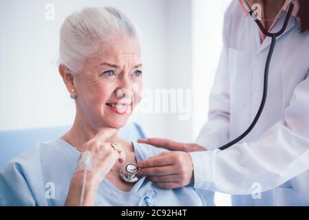 Une patiente âgée heureuse parle avec une femme médecin dans la chambre de l'hôpital. Médecin utiliser le poumon d'écoute du stéthoscope du patient âgé. Soins à domicile concep Banque D'Images