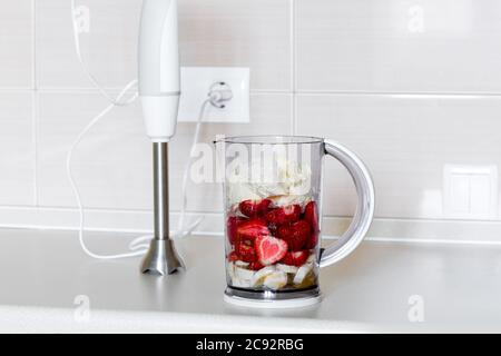 broyage de fruits frais dans un bol mélangeur, fraise avec banane et crème. Banque D'Images
