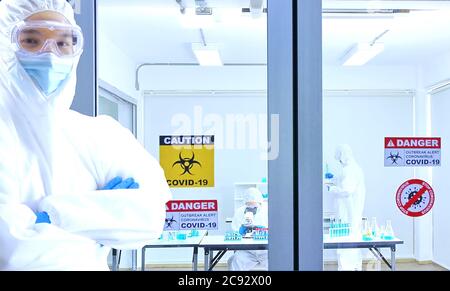 le médecin en costume protecteur debout en laboratoire de virus de face et l'équipe de chercheurs travaillent en laboratoire pour produire le vaccin . Banque D'Images