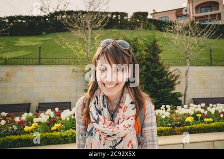 Jeune fille souriante heureuse en chemise rose et foulard ancres avec lunettes de soleil sur la tête et sac à dos orange regardant l'appareil photo à l'extérieur. Un mode de vie sain Banque D'Images