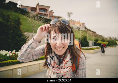 Jeune fille souriante heureuse en chemise rose et foulard ancres avec lunettes de soleil sur la tête et sac à dos orange regardant l'appareil photo à l'extérieur. Un mode de vie sain Banque D'Images