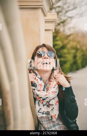 Jeune fille souriante en lunettes de soleil, veste noire et foulard ancres à l'extérieur. Portrait d'une belle femme souriante. Concept de style de vie. Banque D'Images