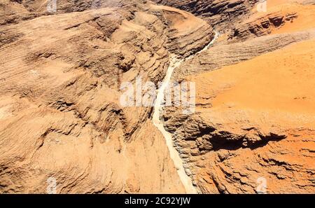 Cours d'eau de lit de rivière séché typique dans un terrain montagneux sombre et aride du désert de Namib avec du sable ocre sur une roche stratifiée sur la côte de Skeleton, Namibie, Afrique du Sud-Ouest Banque D'Images