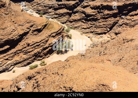 Cours d'eau de lit de rivière séché typique dans un terrain montagneux sombre et aride du désert de Namib avec du sable ocre sur une roche stratifiée sur la côte de Skeleton, Namibie, Afrique du Sud-Ouest Banque D'Images