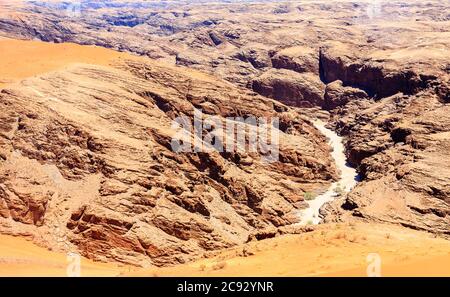 Cours d'eau de lit de rivière séché typique dans un terrain montagneux sombre et aride du désert de Namib avec du sable ocre sur une roche stratifiée sur la côte de Skeleton, Namibie, Afrique du Sud-Ouest Banque D'Images