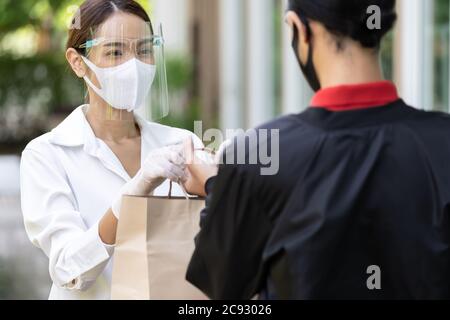 Portrait de femme asiatique atractive donner un sac d'épicerie de boulangerie à l'homme de livraison pour le livrer au client faire la commande en ligne. Concept de service de livraison de nourriture Banque D'Images