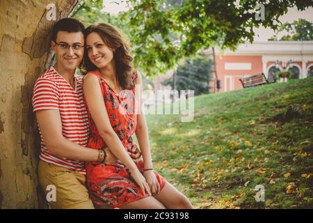 Beau couple amoureux heureux en vêtements rouges sur la nature sous un grand arbre embrassant Banque D'Images