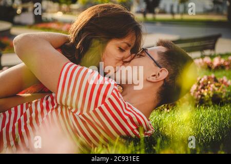 Couple charmant allongé sur l'herbe verte dans le parc, embrassant et passant du temps ensemble Banque D'Images