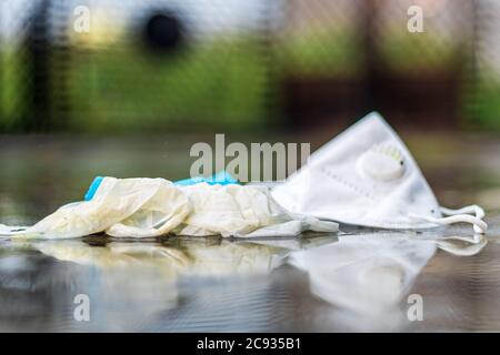 COVID-19 concept de déchets ou de litière. Gants jetés, masque médical et masque N95 jetés après utilisation sous la pluie à l'extérieur. Banque D'Images