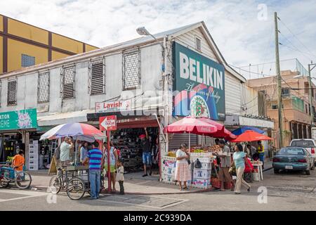 Clients magasinent dans une rue animée avec des magasins et des étals de marché vendant des fruits à Belize City, Caraïbes, Amérique centrale Banque D'Images