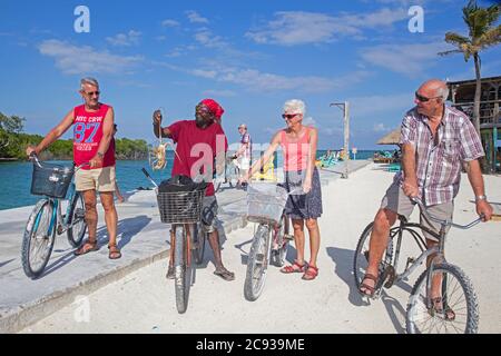 Homme noir local montrant du homard épineux aux touristes occidentaux âgés à vélo sur Caye Caulker / Cayo Caulker, île dans la mer des Caraïbes, Belize Banque D'Images