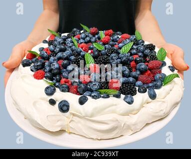 Le dessert de la meringue de Pavlova avec des bleuets, des mûres, des framboises sur une grande assiette blanche dans les mains d'une fille Banque D'Images