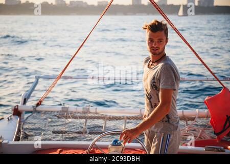 Jeune homme beau, capitaine conduisant un yacht en mer par beau soleil Banque D'Images