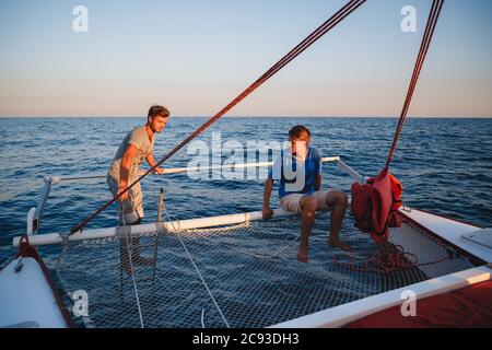 Deux jeunes hommes beaux à l'arrière du voilier se préparant à la plongée, capitaine pilotant le yacht en mer à la journée ensoleillée Banque D'Images