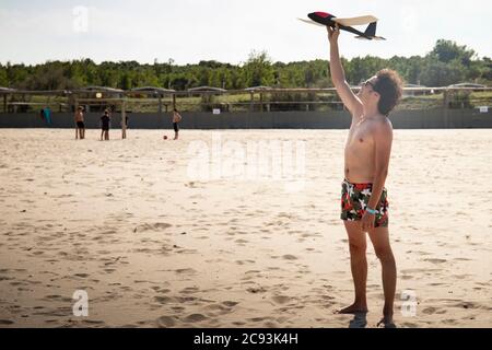 Jeune homme, portant un maillot de bain, jetant un avion ou un planeur sur la plage en été. Arrière-plan ou fond d'écran avec espace de copie. Rosolina mare, Vénétie, I Banque D'Images