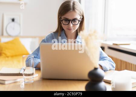 Travailler à la maison me permet de travailler de façon flexible. Agréable bonne jeune femme freelance travaillant sur ordinateur à la maison. Banque D'Images