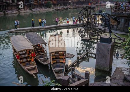 Feng Huang, Chine - août 2019 : vieux bateaux de tourisme en bois historiques amarrés sur la rive de la rivière Tuo à côté de l'ancien moulin à bois roue Banque D'Images