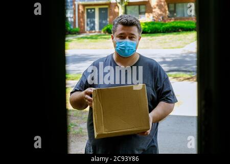 Liveur portant un masque facial donnant une boîte en carton à l'entrée de la livraison à domicile pendant la quarantaine de la pandémie du coronavirus. Banque D'Images
