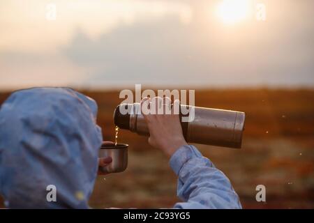 Voyageur fille versant le thé de thermos tasse, à l'extérieur. Jeune femme buvant à la tasse. Voyage à thème. Toundra d'automne. Banque D'Images