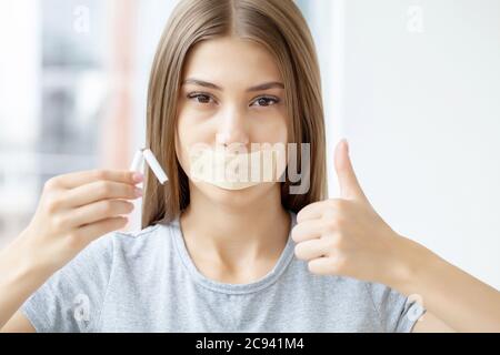 Arrêtez de fumer, une femme avec une bouche scellée tenant une cigarette cassée Banque D'Images